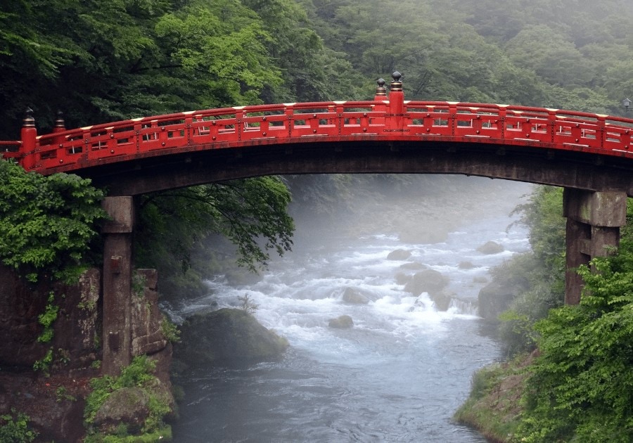 Shinkyo Bridge in Japan, a red bridge hanging between green grasses with some gold ornaments in Nikko Japan