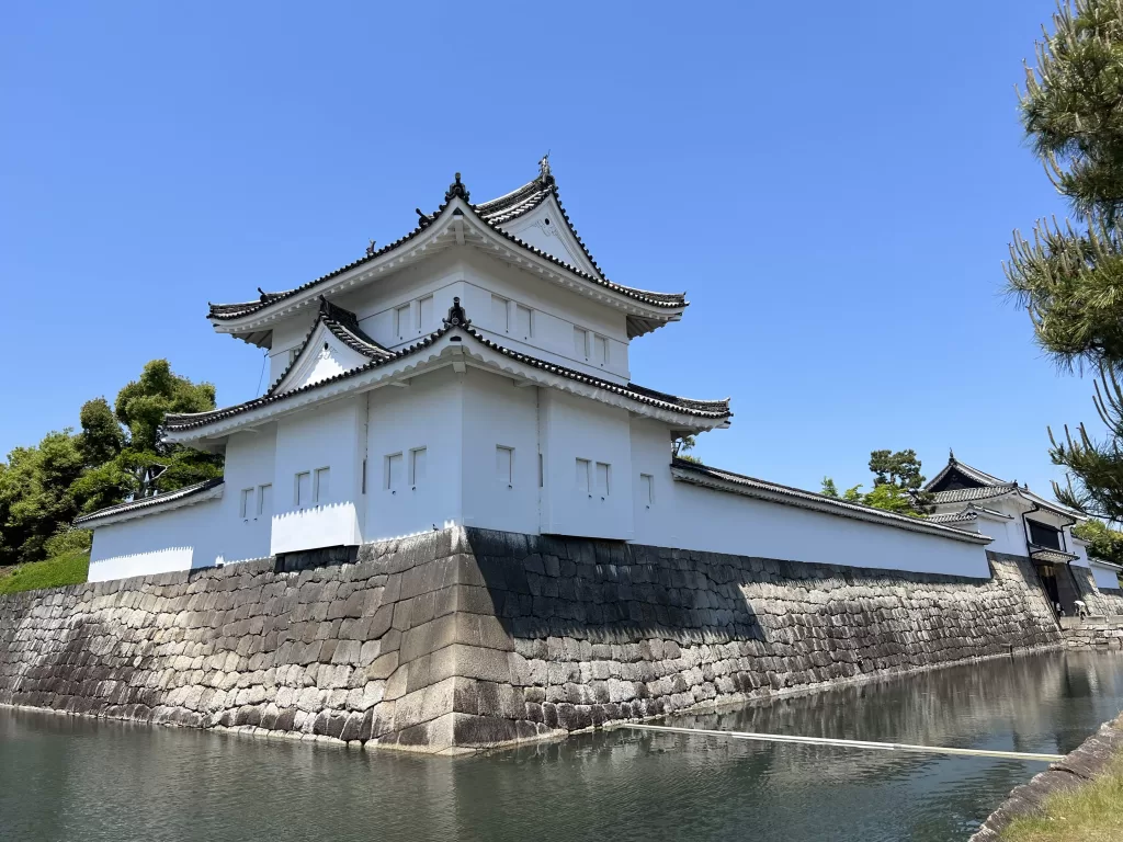 A Japanese castle staning on a river with stone base surrounded by some gren treas, located in Nakagyo, one of the most expensive areas in Kyoto